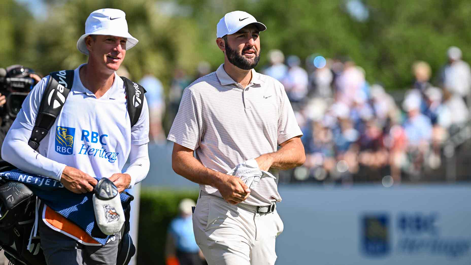 Scottie Scheffler smiles as he walks with caddie Ted Scott off the first tee during the first round of the RBC Heritage at Harbour Town Golf Links on April 17, 2025 in Hilton Head Island, South Carolina.